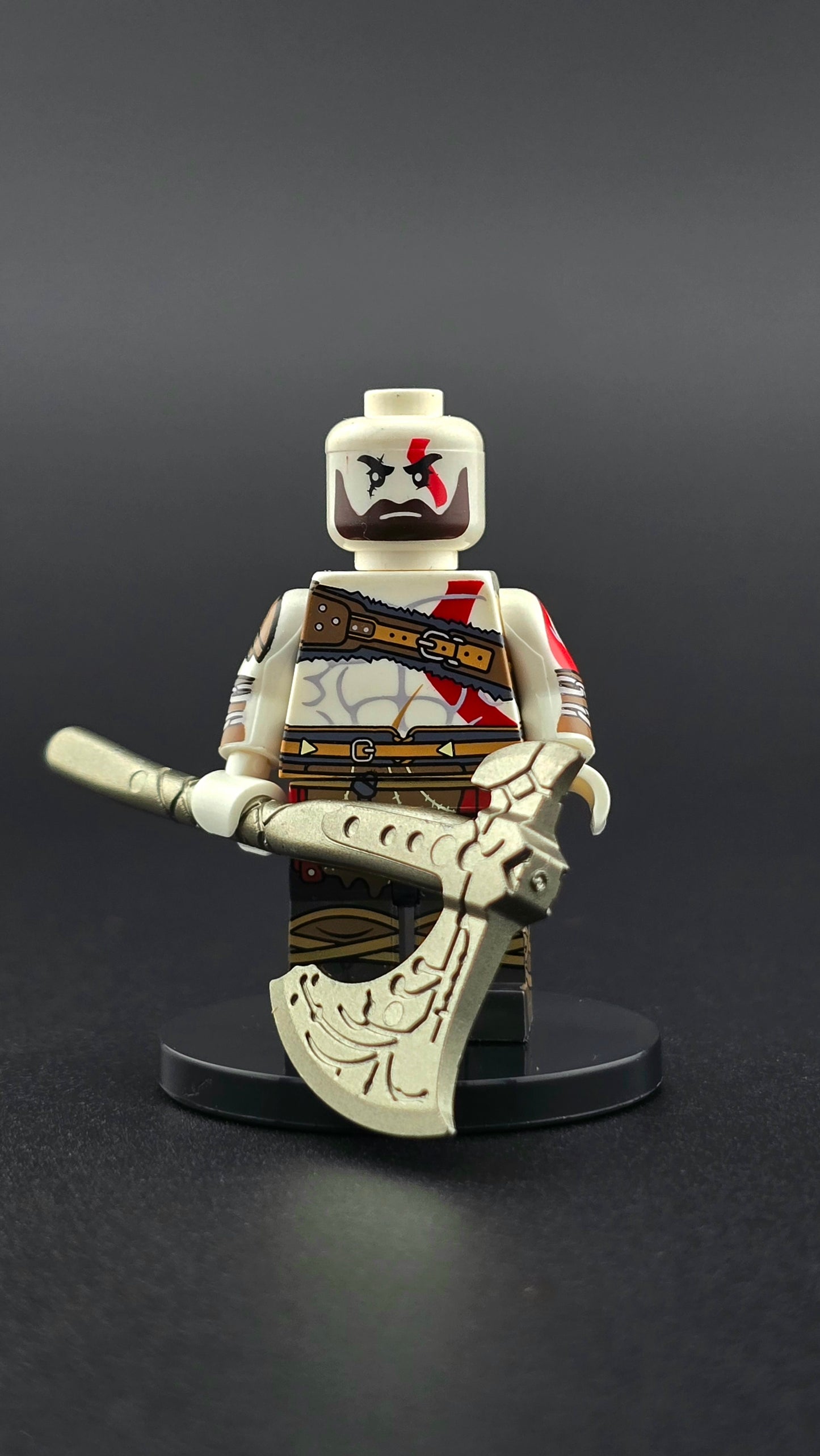 Custom gaming inspired Kratos minifigure with grey and red Norse attire, muscular build, beard, tattoos, and Viking axe accessory. Detailed mythological warrior design compatible with leading brick style building sets.