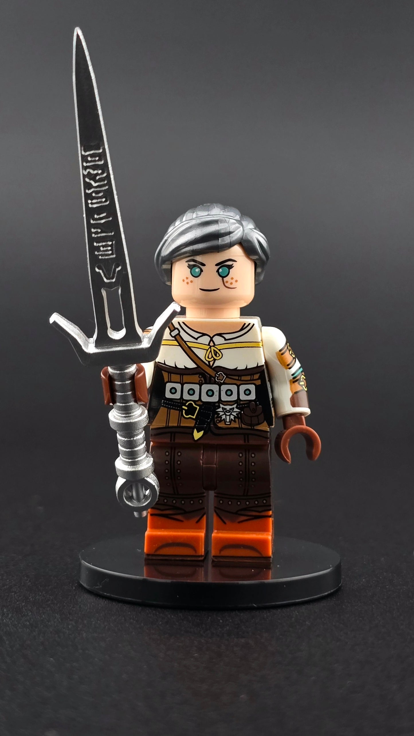Custom gaming inspired Ciri minifigure with silver hair, intricate white and grey outfit printing, and silver sword accessory. Detailed fantasy warrior design compatible with leading brick style building sets.