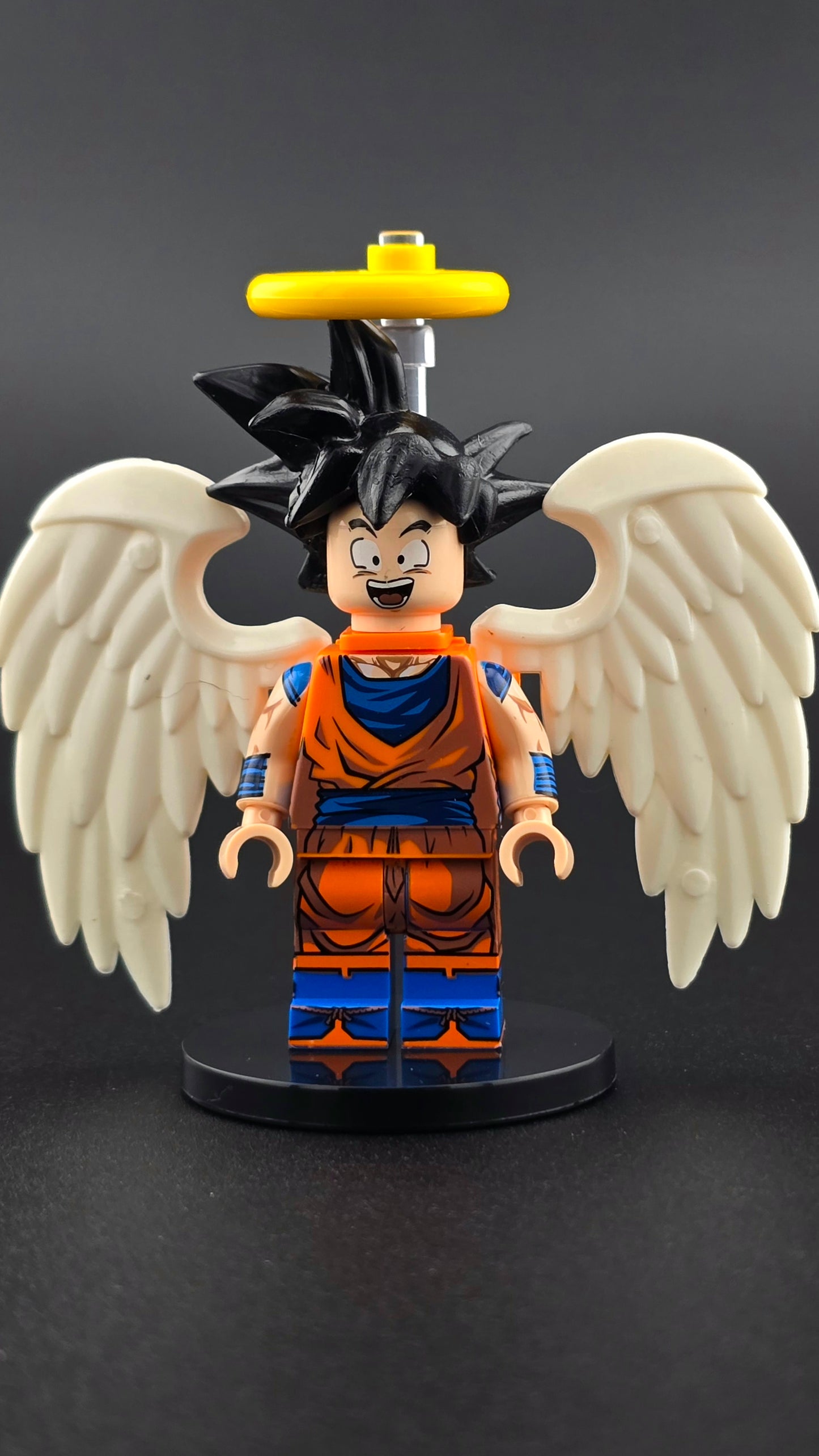 Custom anime inspired Goku minifigure in orange and blue with spiky hair, white wings, halo, and cheerful expression. Detailed celestial fighter design compatible with leading brick style building sets.