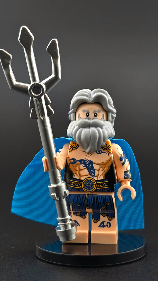 Custom Poseidon inspired minifigure with gray hair, beard, blue tattoos, and a flowing blue cape, holding a silver trident. Detailed print and compatible with leading brick-style building systems.