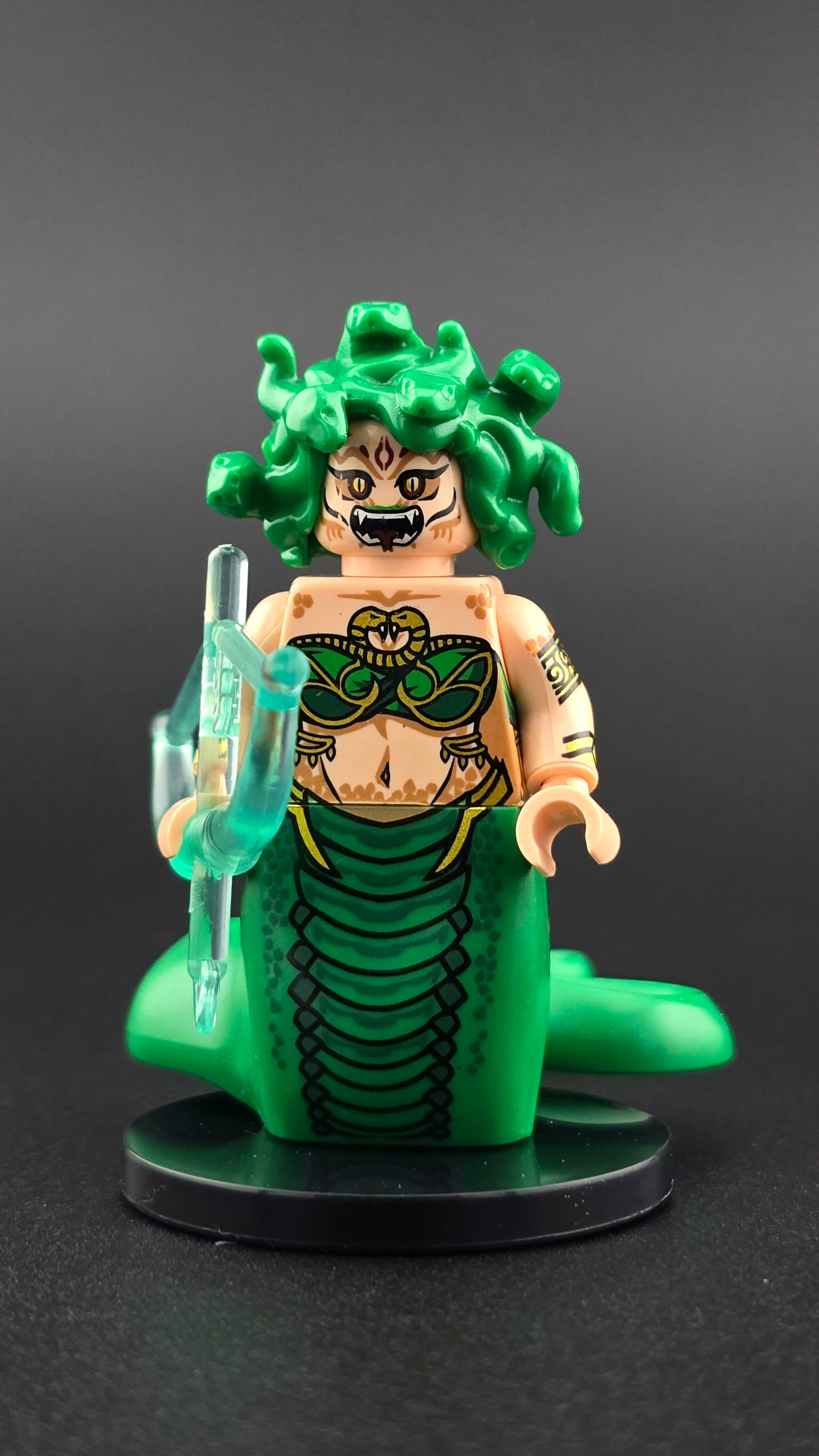 Custom mythology-inspired Medusa minifigure with green snake hair, golden snake eyes, intricate printed snake body, and translucent magical bow. Detailed, vibrant design compatible with major brick-style building systems.