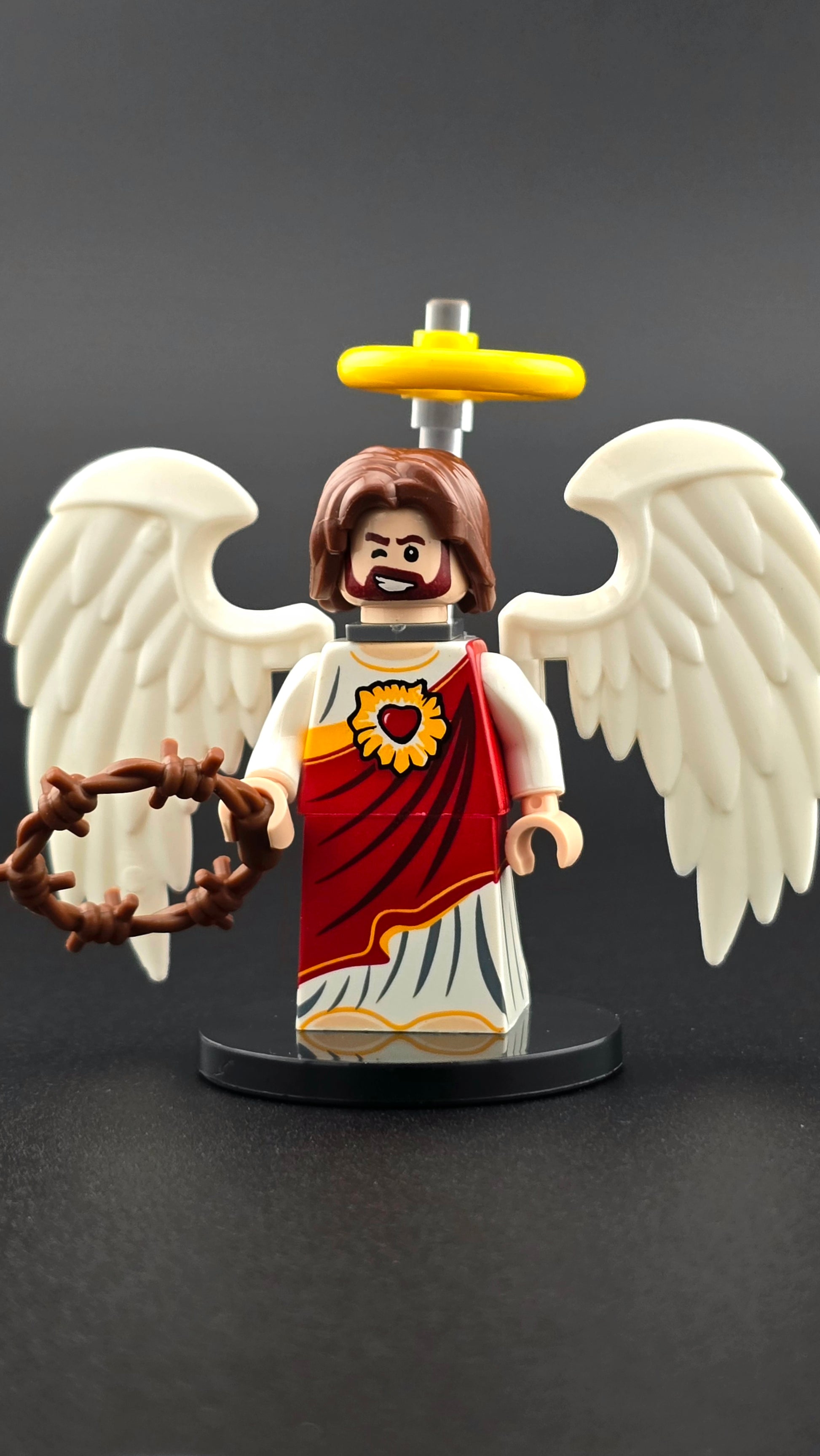 Custom religion-inspired resurrected figure with smiling, winking expression, red and white clothing, golden halo, white wings, and wreath accessory. Features symbolic colors and detailed elements compatible with leading brick-style building systems.