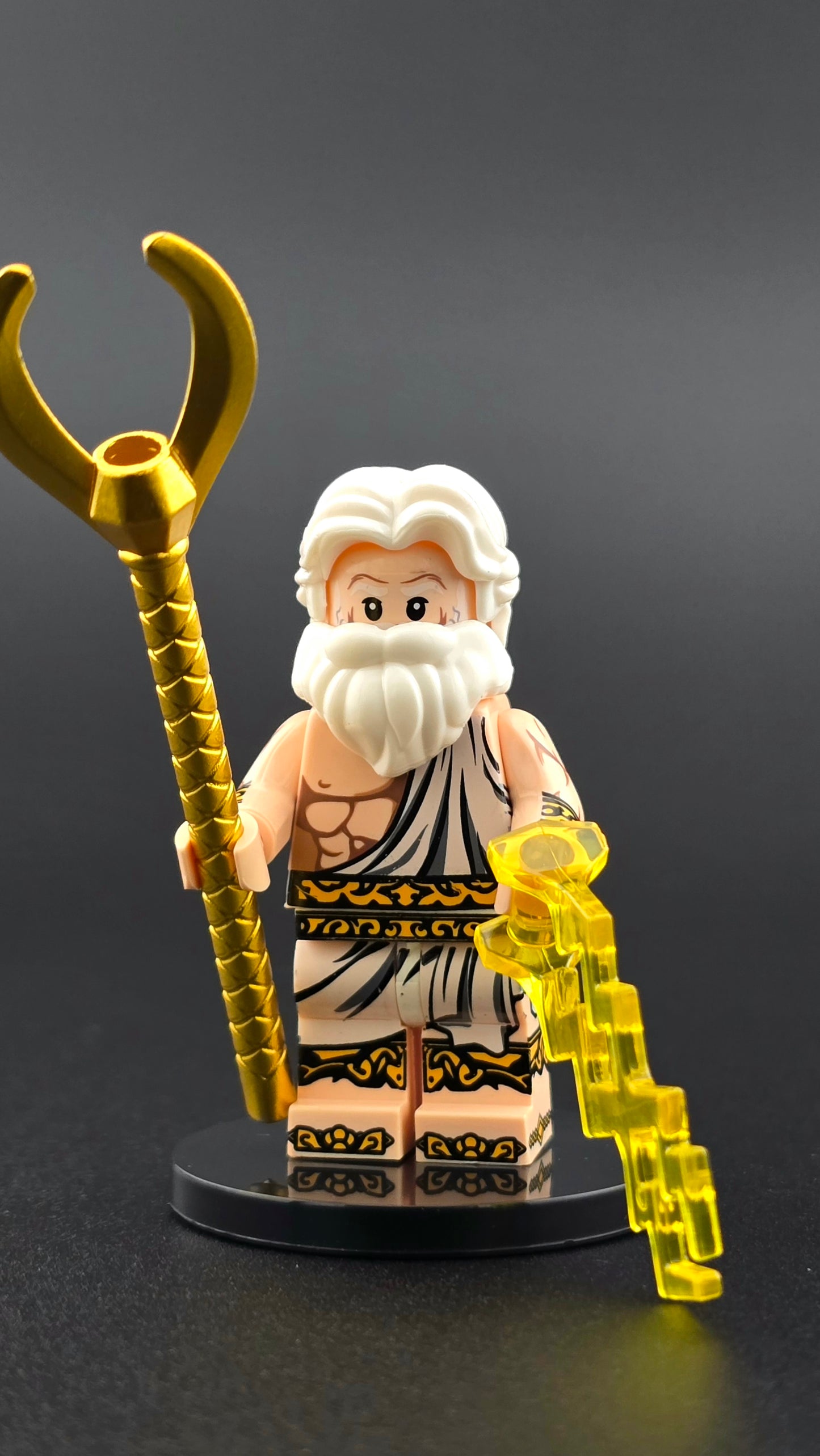 Custom mythology-inspired Zeus minifigure with white beard and hair, wearing a white toga accented with gold, holding a lightning bolt and golden staff. Features a regal design and detailed accessories compatible with leading brick-style systems.