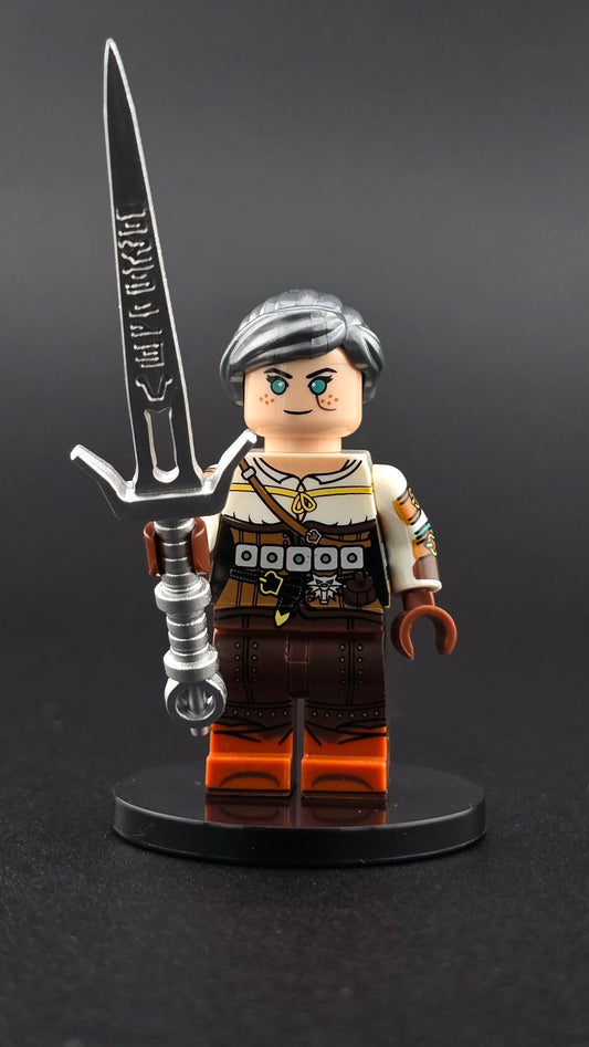 Custom gaming inspired Ciri minifigure with silver hair, intricate white and grey outfit printing, and silver sword accessory. Detailed fantasy warrior design compatible with leading brick style building sets.