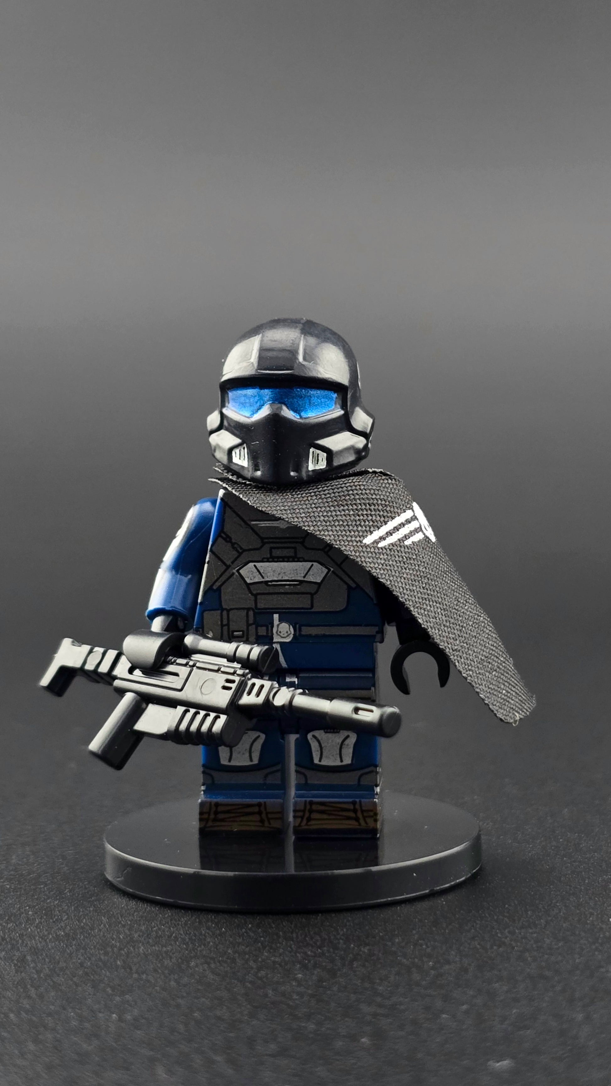 Custom gaming inspired Helldiver minifigure in blue and black armor with helmet, assault rifle, and shoulder cape. Detailed sci fi soldier design compatible with leading brick style building sets.