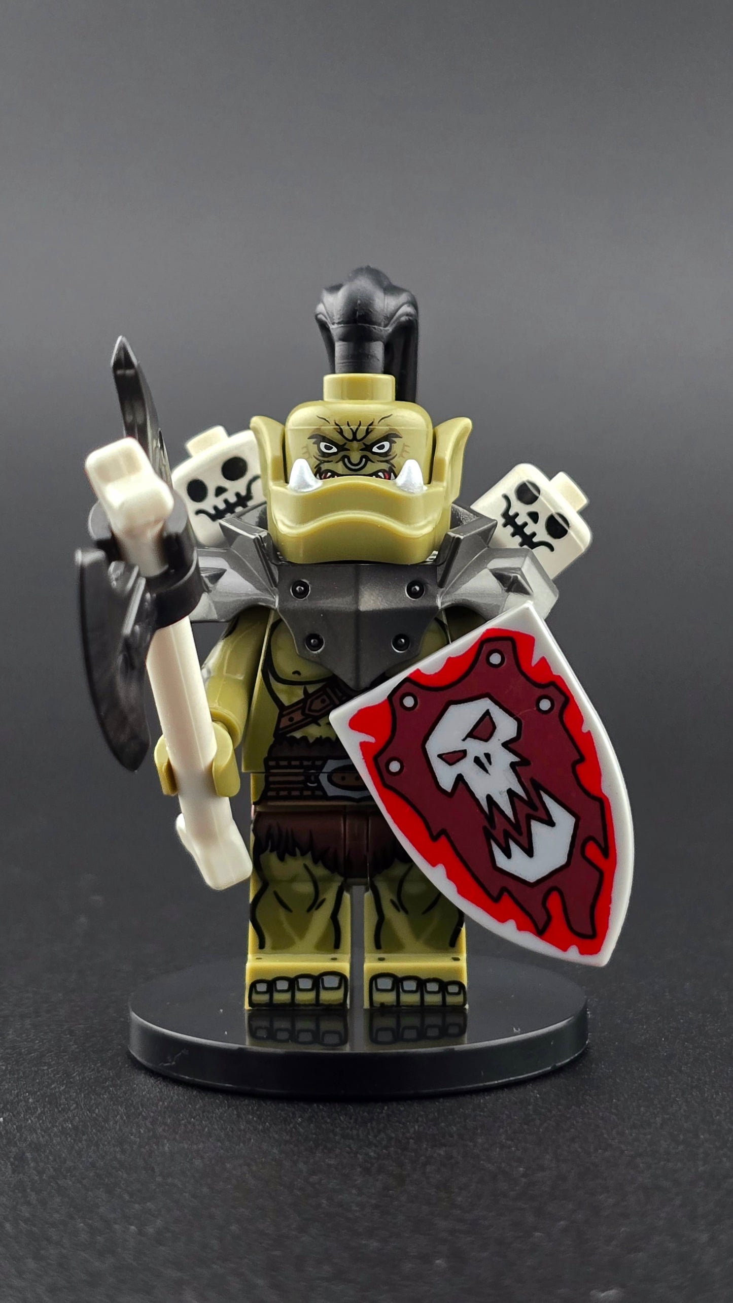 Custom fantasy inspired Orc Warlord minifigure with green skin, silver heavy shoulder armor, skulls on spikes, bone axe, and shield. Designed with fierce chieftain styling compatible with leading brick style building sets.