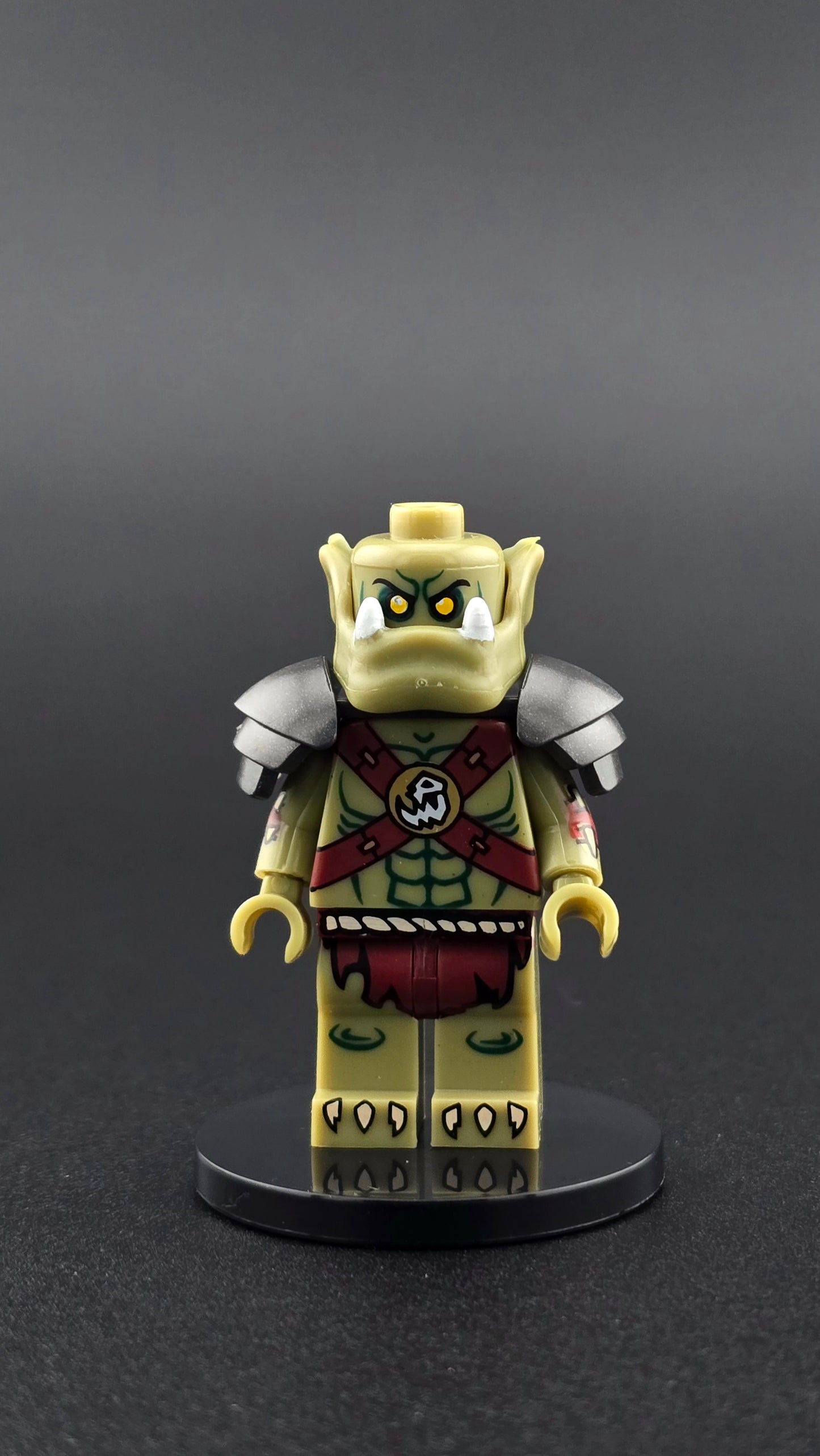 Custom fantasy inspired Orc Footman minifigure with green skin, red armor, muscular build, and heavy pauldrons. Designed for epic battle displays and compatible with leading brick style building sets.
