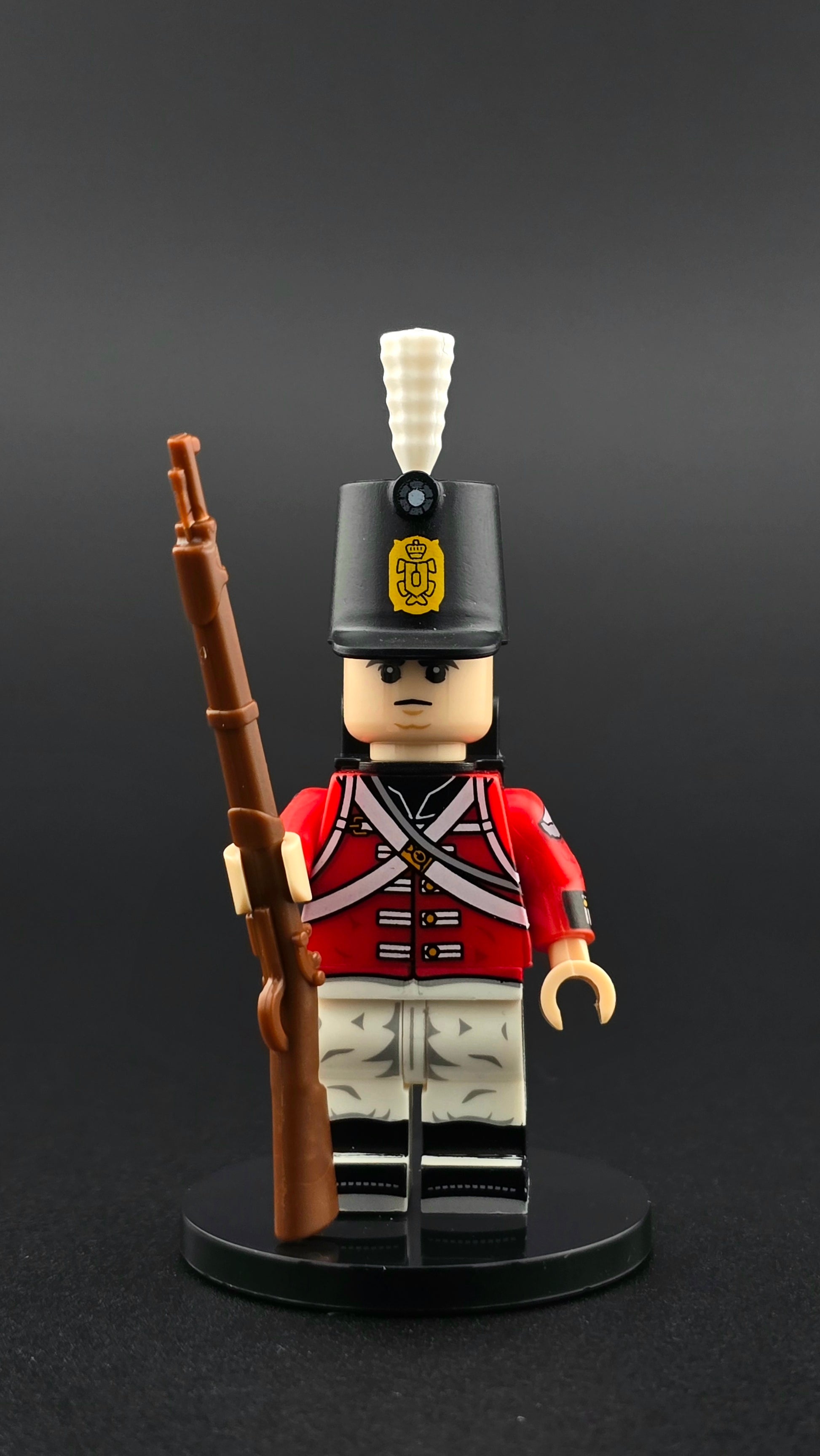 Custom British Napoleonic Soldier minifigure in red, white, and black uniform with shako and white plume, equipped with rifle and backpack accessories, compatible with leading brick-style building systems.