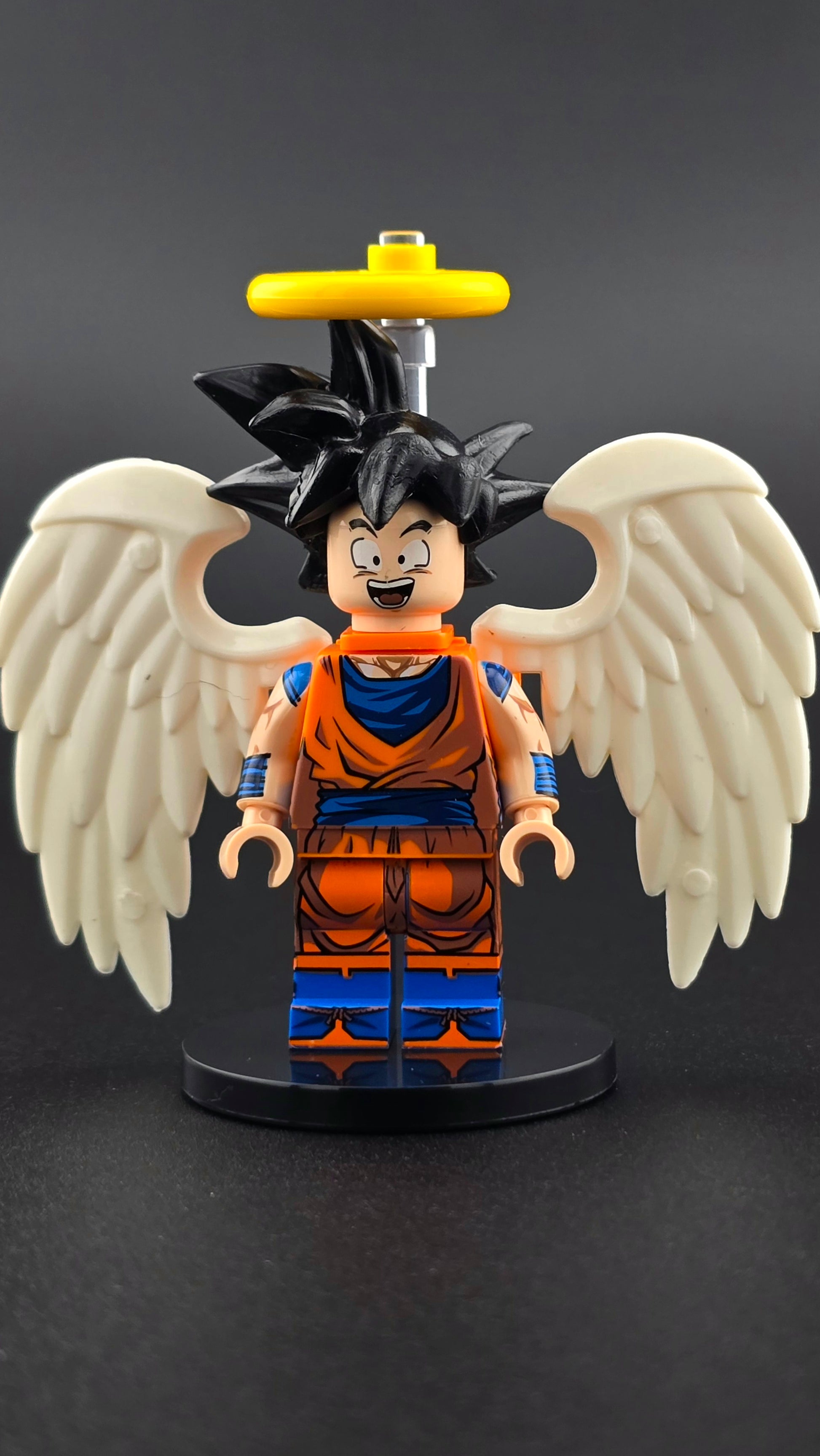 Custom anime inspired Goku minifigure in orange and blue with spiky hair, white wings, halo, and cheerful expression. Detailed celestial fighter design compatible with leading brick style building sets.