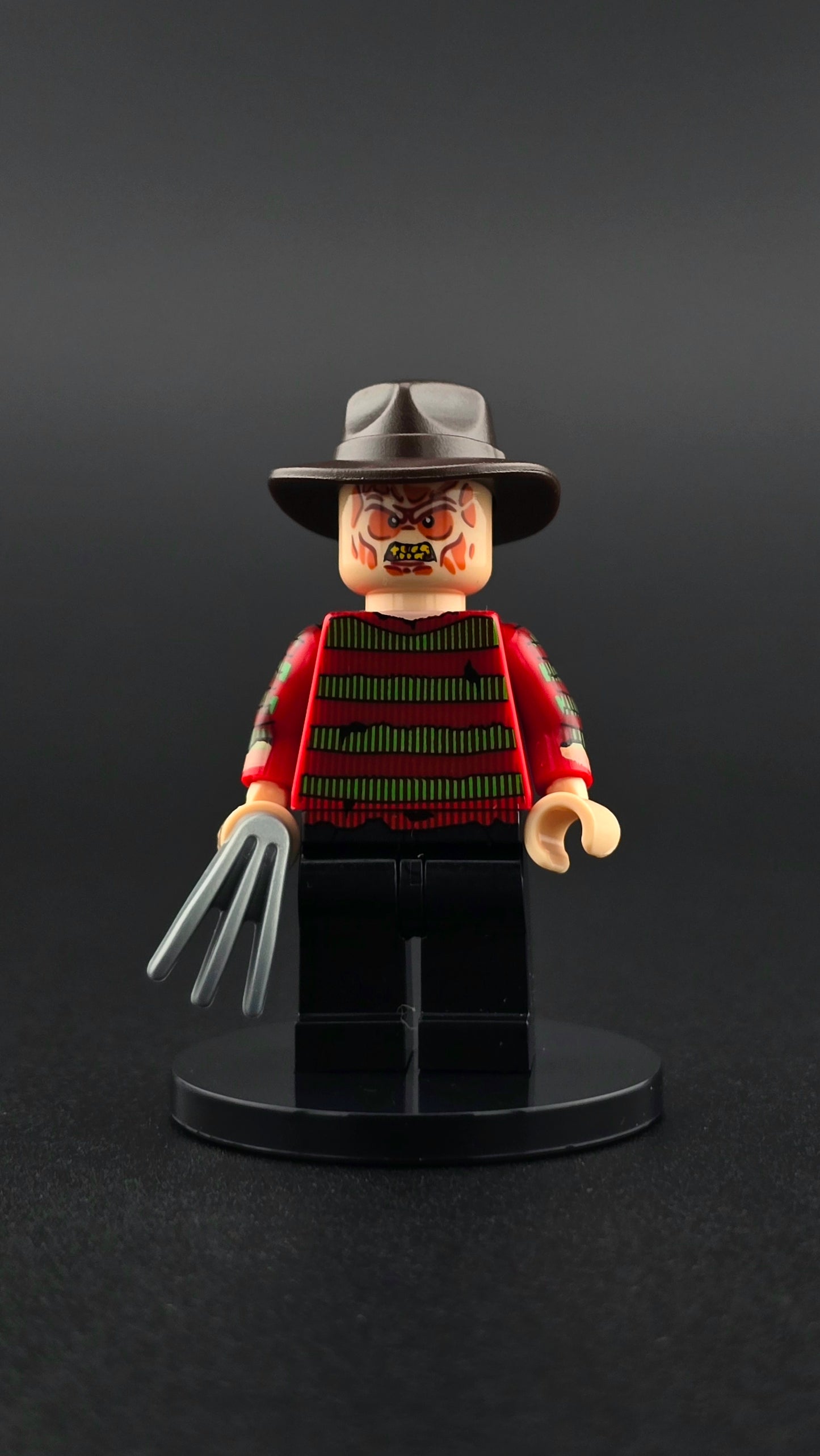 Custom horror inspired minifigure in red and black with sinister expression and razor claw accessory. Detailed villain themed design compatible with leading brick style building sets.
