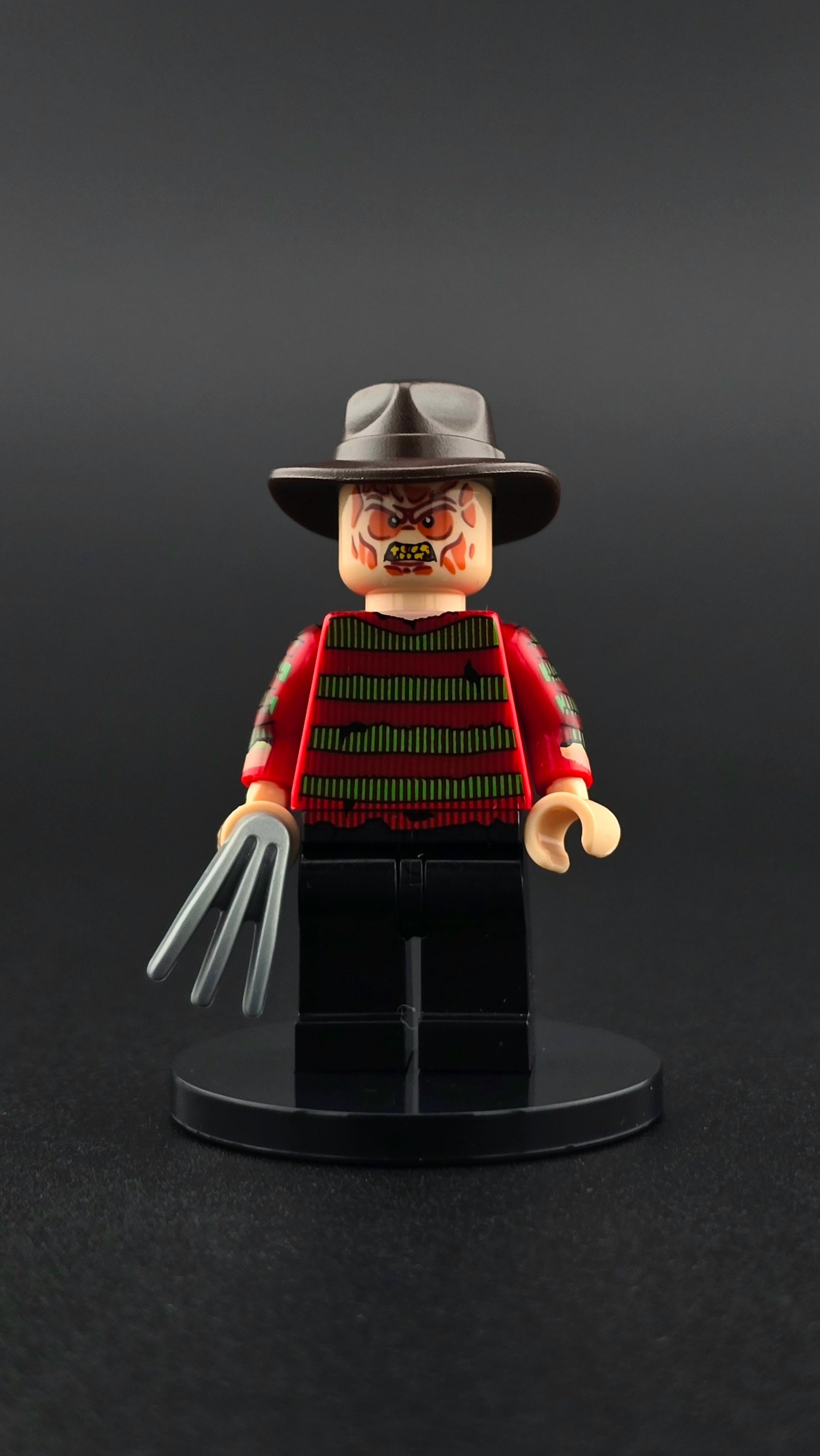 Custom horror inspired minifigure in red and black with sinister expression and razor claw accessory. Detailed villain themed design compatible with leading brick style building sets.