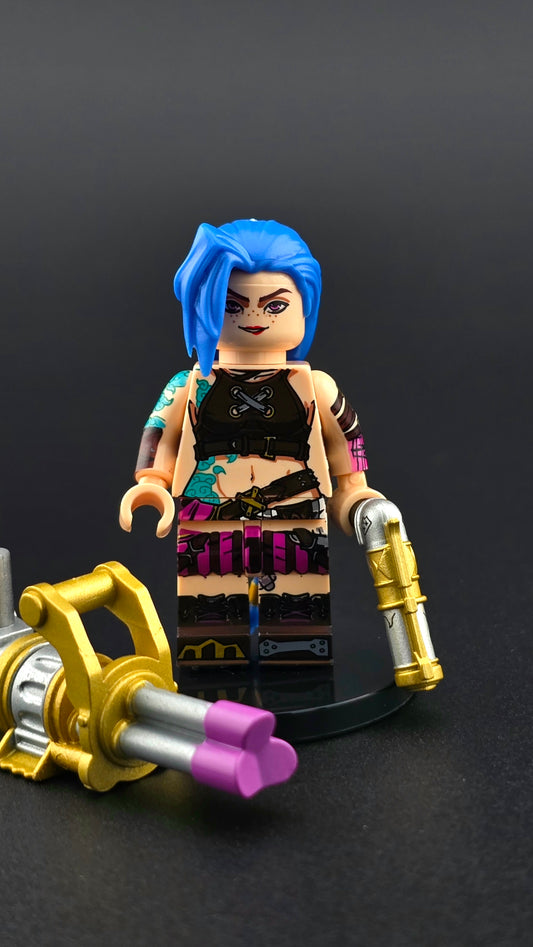 Custom TV inspired Jinx style minifigure with bright blue and pink details, gold accents, and snarky expression, holding a gatling gun and pistol. Vibrant premium design compatible with leading brick style building sets.
