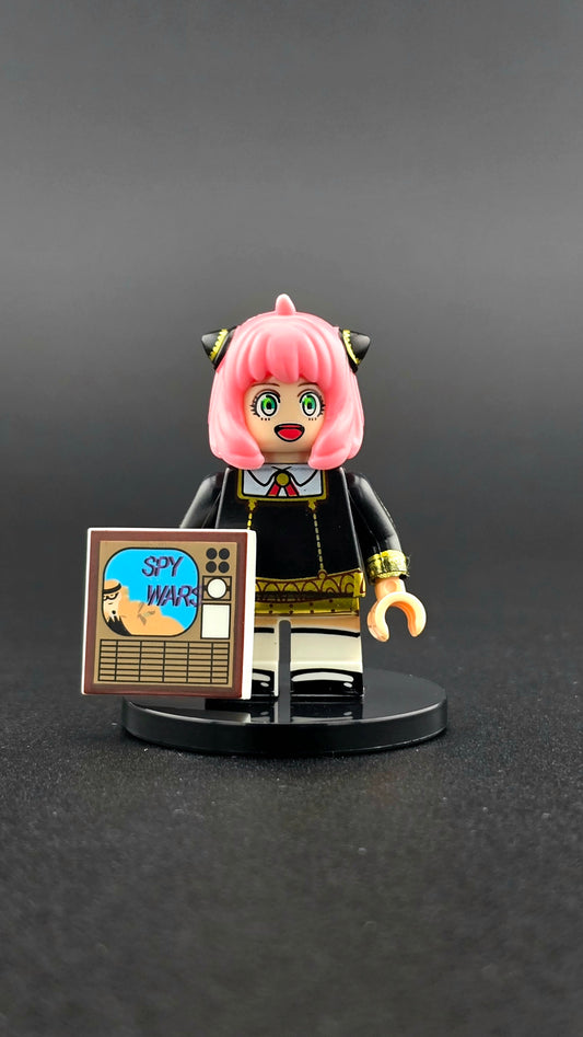 Custom anime-inspired Anya Forger minifigure with pink hair, school outfit, and Spy Wars TV cover accessory, based on Spy X Family and compatible with leading brick-style building systems.
